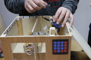 Eine Hand setzt einen Mikrocontroller mit Kabeln in eine Holzkiste.