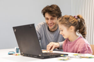 Ein Mann und ein junges Mädchen sitzen an einem Laptop und lachen.
