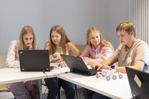 Vier Jugendliche sitzen an zwei Laptops. Sie schauen konzentriert und lachen.