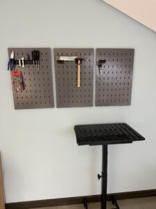 An einer Wand sind unterschiedliche Werkzeuge befestig. Davor steht ein kleiner Tisch.