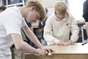 Zwei Jungen stehen um einen Werktisch. Mit Schleifpapier schleifen sie an Bumerangs aus Holz.