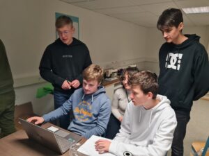 Fünf Jugendliche sitzen vor einem Laptop und schauen konzentriert.