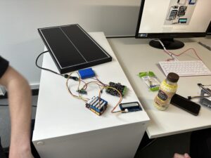 Das Photovoltaikmodul ist mit Kabeln an einem Bildschirm, einem Mikrocontroller, einem Laderegler und weiteren Komponenten angeschlossen.